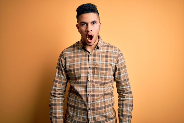 Young handsome man wearing casual shirt standing over isolated yellow background afraid and shocked with surprise and amazed expression fear and excited face