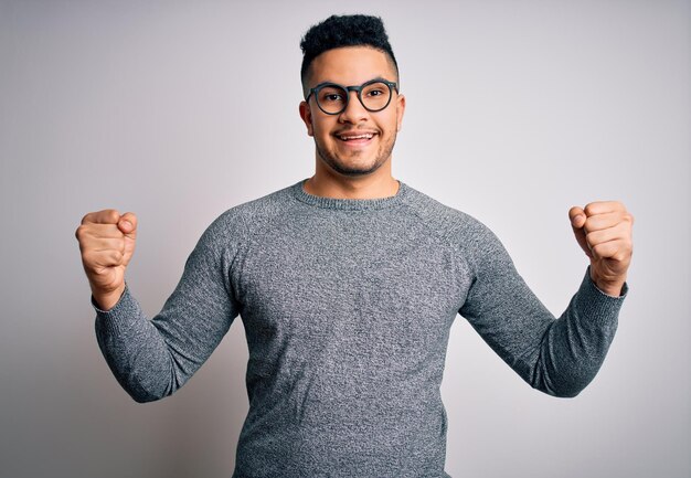 Young handsome man wearing casual sweater and glasses over isolated white background celebrating surprised and amazed for success with arms raised and open eyes Winner concept