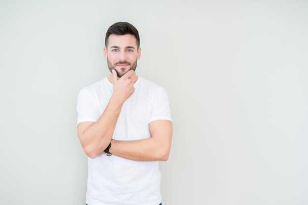 Young handsome man wearing casual white tshirt over isolated background looking confident at the camera with smile with crossed arms and hand raised on chin Thinking positive