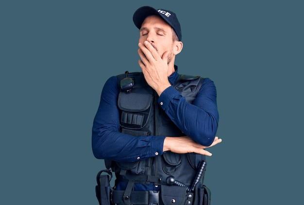 Молодой красивый мужчина в полицейской форме скучно зевает, прикрывая рот рукой. беспокойство и сонливость.