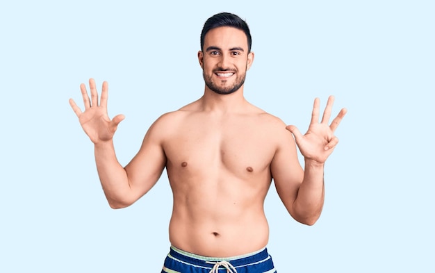 Young handsome man wearing swimwear showing and pointing up with fingers number nine while smiling confident and happy.