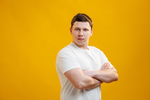 Photo young handsome man wearing white tshirt with crossed arms looking at the camera over yellow studio background