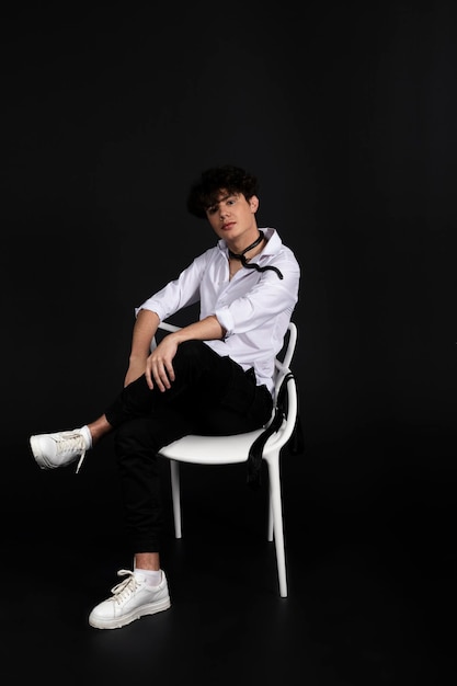 Young handsome man in a white shirt sitting on a chair with a black snake crawling around his neck Isolated on black background