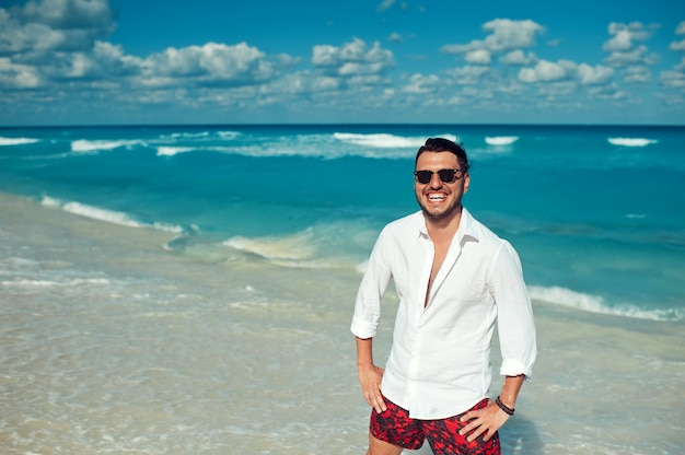 Young handsome man in white shirt and sunglasses enjoying day on the beach