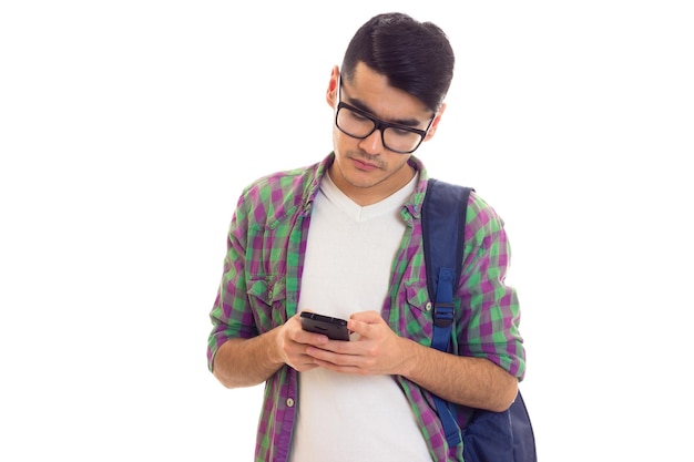 스마트폰을 사용하여 흰색 티셔츠와 파란색 배낭이 달린 체크무늬 셔츠를 입은 젊고 잘생긴 남자