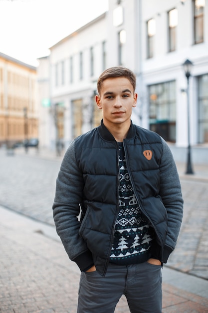 Photo young handsome man in winter clothes standing near the building, holding hands in pockets