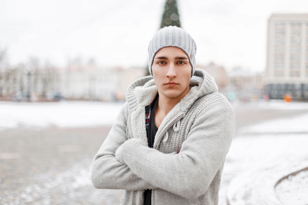 Young handsome man in winter knit sweater and hat is in the city on a snowy day