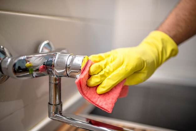 Young handsome man wiping faucet in kitchen. House cleaning service or husband doing chores