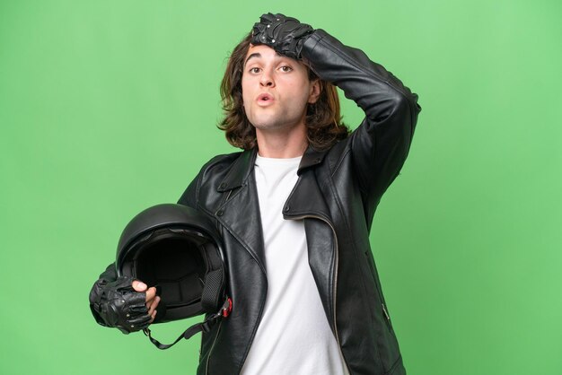 Фото Молодой красивый мужчина в мотоциклетном шлеме на зеленом цветном фоне делает неожиданный жест, глядя в сторону