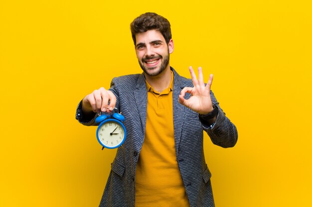 Young handsome man with an alarm clock against orange background