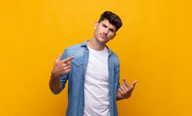 Young handsome man with a bad attitude looking proud and aggressive, pointing upwards or making fun sign with hands