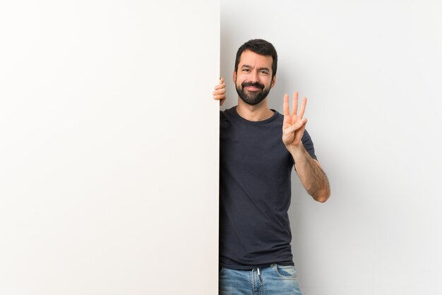 Young handsome man with beard holding a big empty placard happy and counting three with fingers