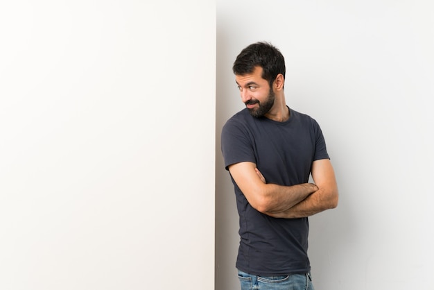 Photo young handsome man with beard holding a big empty placard with arms crossed and happy