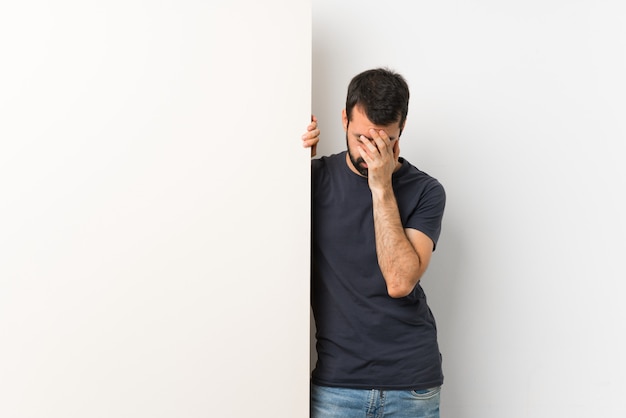 Young handsome man with beard holding a big empty placard with tired and sick expression