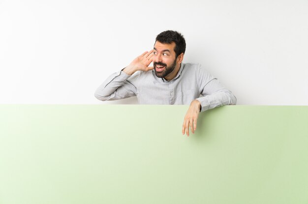 Young handsome man with beard holding a big green empty placard 