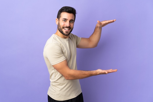 Young handsome man with beard over isolated background holding copyspace to insert an ad