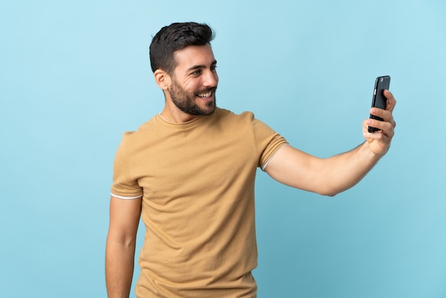 Young handsome man with beard over isolated background making a selfie