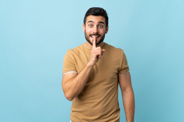 Young handsome man with beard over isolated background showing a sign of silence gesture putting finger in mouth