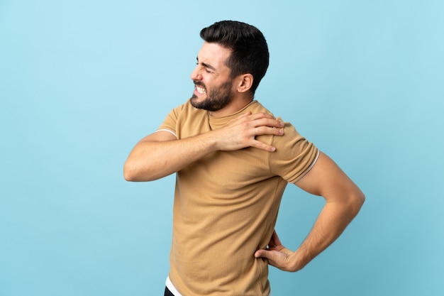 Young handsome man with beard over isolated background suffering from pain in shoulder for having made an effort