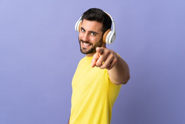 Giovane uomo bello con la barba isolata su musica d'ascolto della parete viola e che indica la parte anteriore