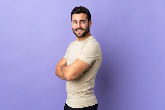 Young handsome man with beard over isolated wall looking to the side and smiling