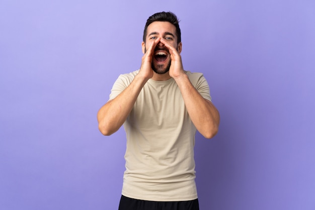 Young handsome man with beard over isolated wall shouting and announcing something