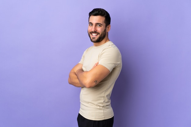 Young handsome man with beard over isolated wall with arms crossed and happy