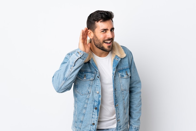 Photo young handsome man with beard isolated on white listening to something by putting hand on the ear