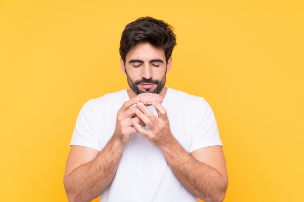 Giovane uomo bello con la barba sopra la parete gialla isolata che tiene una ciambella