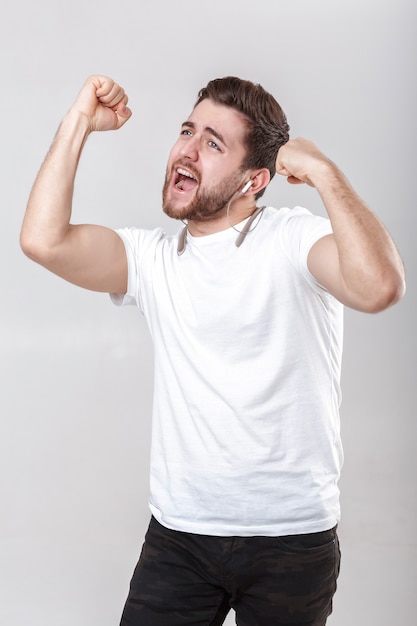 ヘッドフォンで音楽を聴いてTシャツのひげを持つ若いハンサムな男