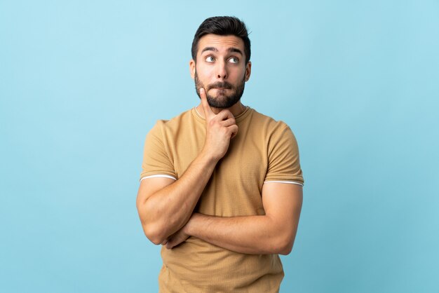 Young handsome man with beard over wall having doubts and thinking