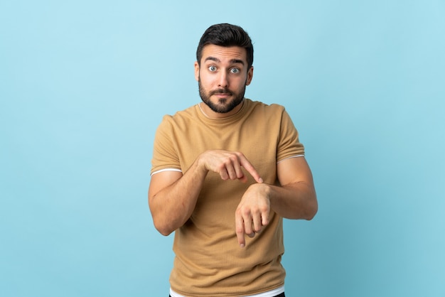 Young handsome man with beard over wall making the gesture of being late