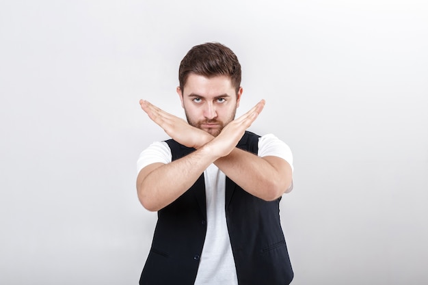 Il giovane bell'uomo con la barba in una camicia bianca e un gilet nero mostra il gesto di fermarsi