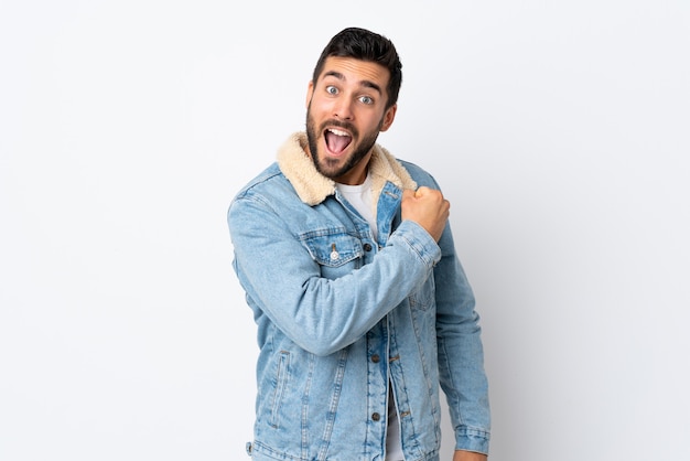 Young handsome man with beard on white wall celebrating a victory