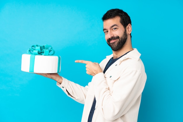 Young handsome man with a big cake over isolated blue wall