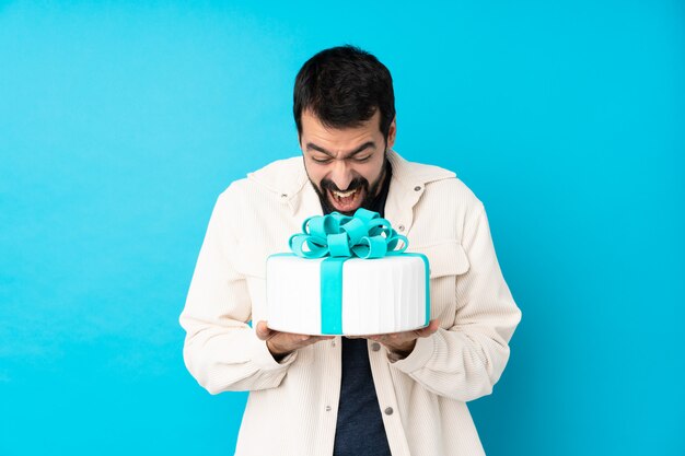 Young handsome man with a big cake over isolated blue wall