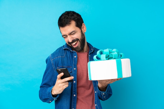 Giovane uomo bello con una grande torta con il telefono in posizione di vittoria