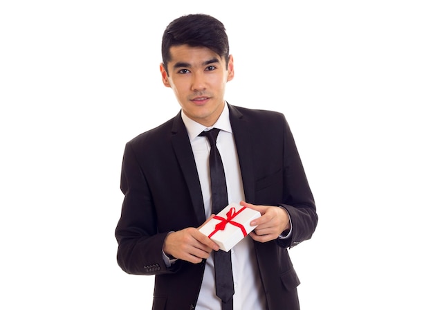 Young handsome man with black hair in white shirt and black suit with tie holding a present on white background