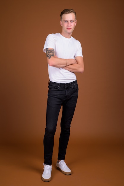 Young handsome man with blond hair against brown wall