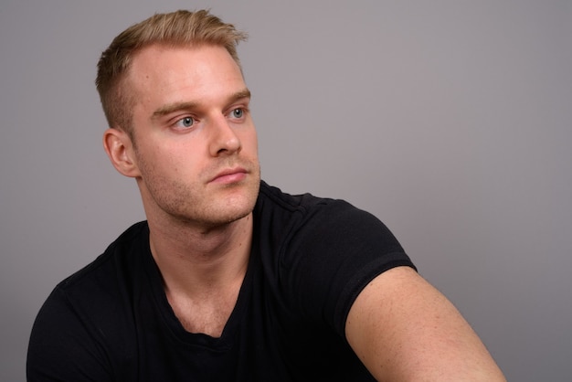 Young handsome man with blond hair against gray