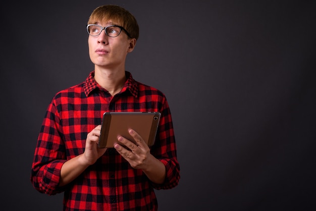 Young handsome man with blond hair thinking and using digital tablet