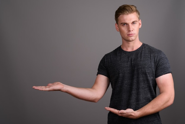 Photo young handsome man with blond hair wearing gray shirt on grey wall