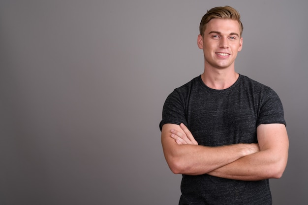 Young handsome man with blond hair wearing gray shirt on grey wall