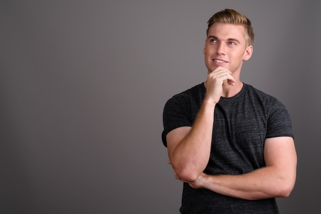 Young handsome man with blond hair wearing gray shirt on grey wall