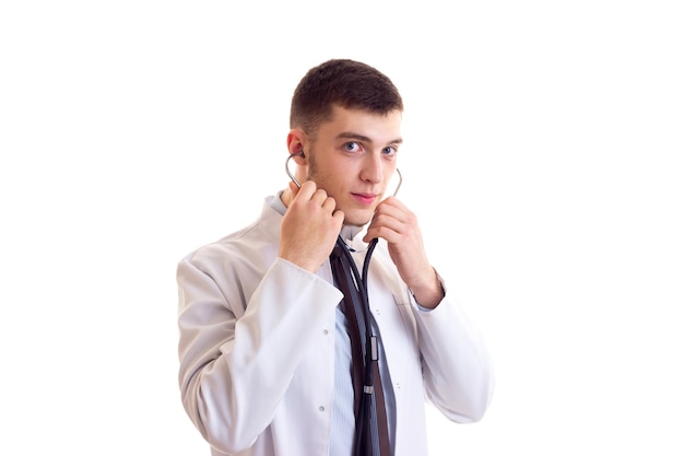 Young handsome man with brown hair in blue shirt tie and doctor gown using stethoscope in studio