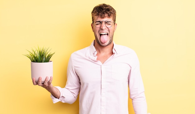Young handsome man with cheerful and rebellious attitude, joking and sticking tongue out. decorative plant concept