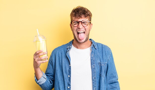 young handsome man with cheerful and rebellious attitude, joking and sticking tongue out. milkshake concept