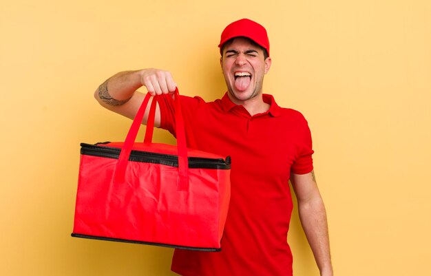 Young handsome man with cheerful and rebellious attitude joking and sticking tongue out pizza courier concept