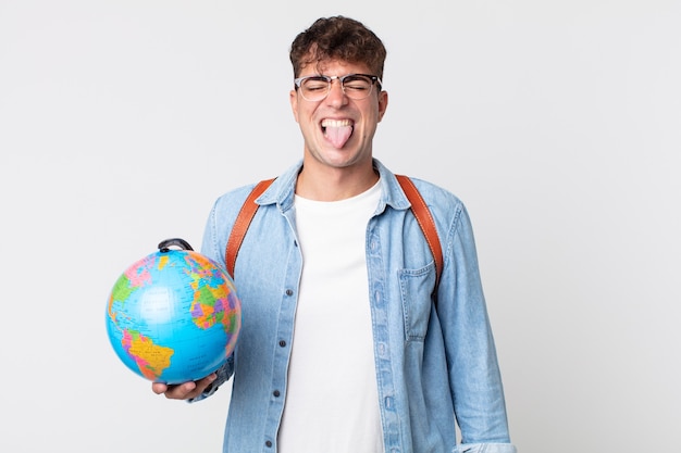 陽気で反抗的な態度、冗談を言って舌を突き出している若いハンサムな男。世界の地球地図を持っている学生