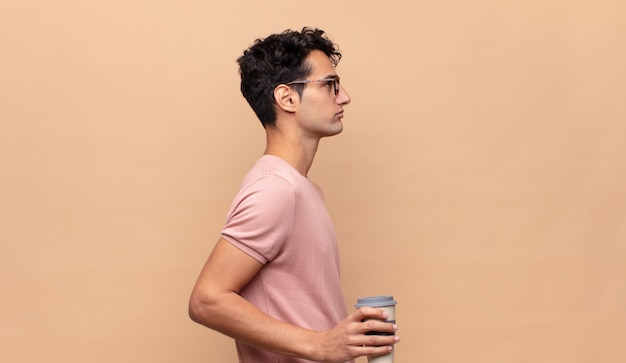 Photo young handsome man with a coffee on profile view looking to copy space ahead, thinking, imagining or daydreaming
